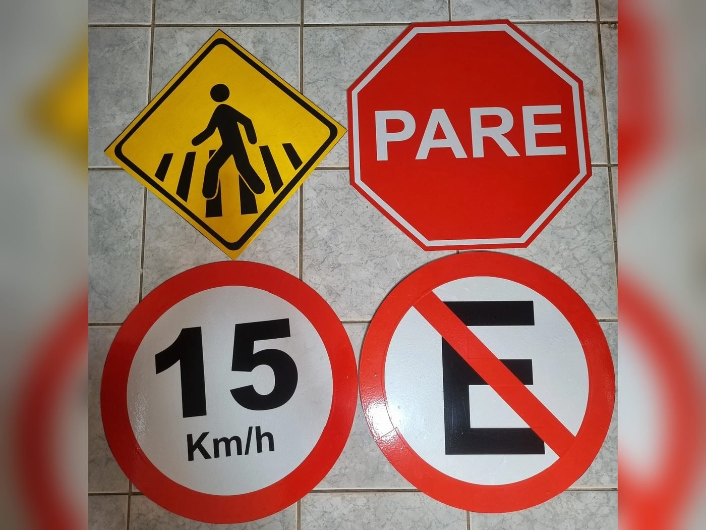 Placas de trânsito fabricadas pela Belplac: PARE (R-1), velocidade máxima 15 km/h (R-19), proibido estacionar (R-6a) e travessia de pedestres
